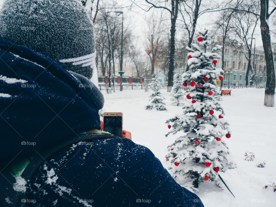 man photographs the snow-covered Christmas tree with toys