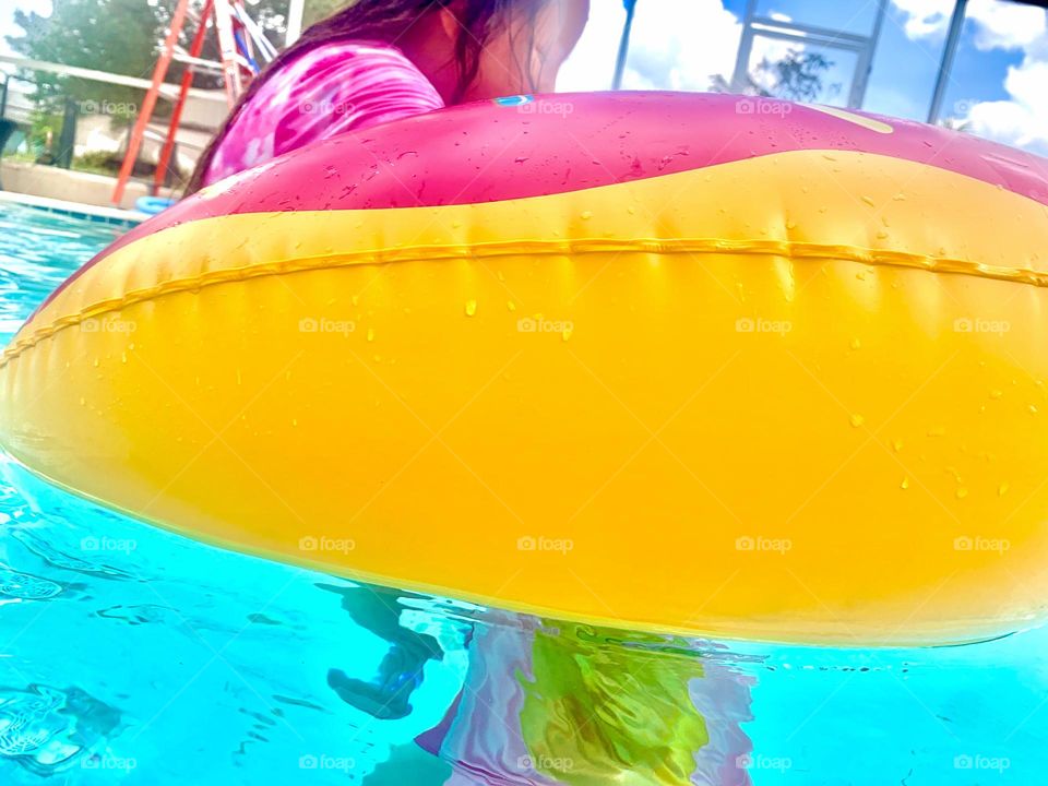 Children Having Fun In The Pool Swimming And Playing With The Yellow And Pink Donut Floaty In The Outdoor Enclosure.