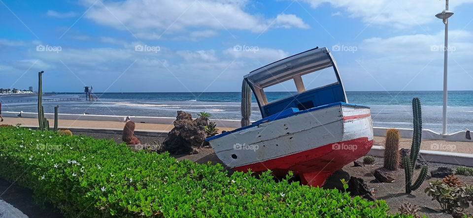 Paisaje de barco en tierra con vegetación y playa de fondo en día nublado
