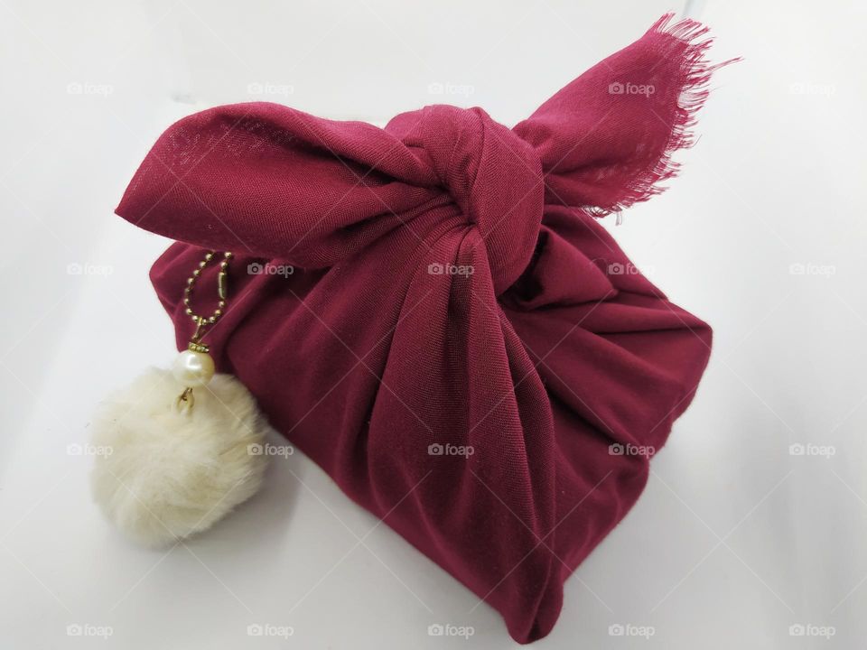 A gift wrapped in a red cloth.  Adorned with a white fluffy ball hanger.  Birthday gifts.  Isolated on a white background.