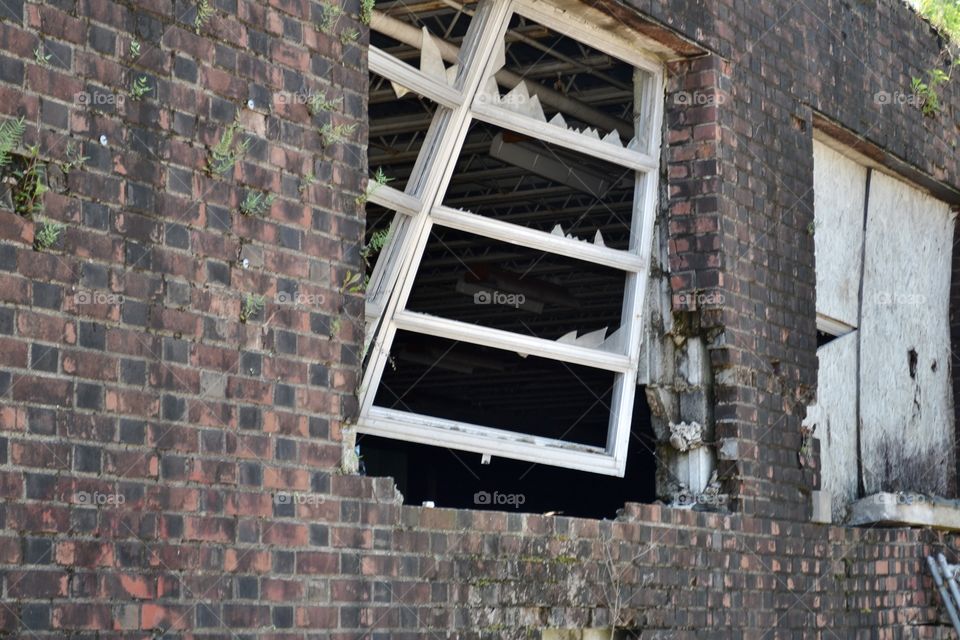 A broken window hanging ajar in an old dirty brick wall