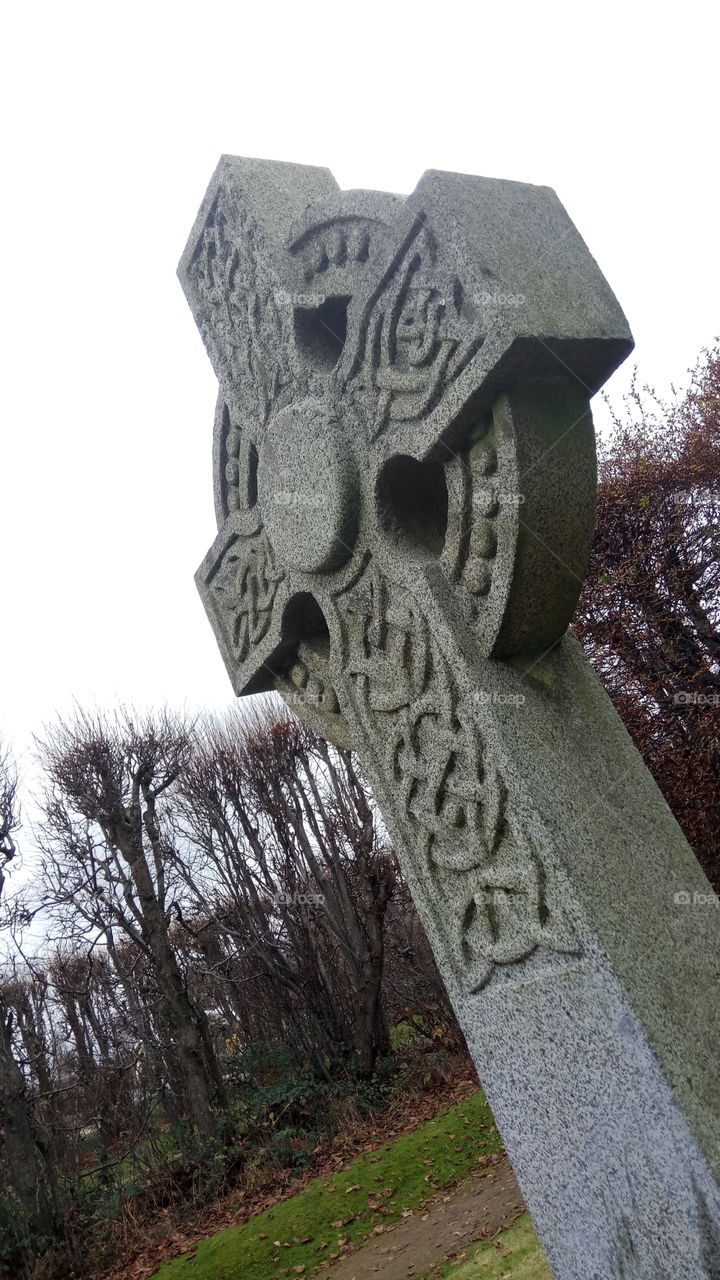 A lonely celtic cross surrounded by a dark forest in North Ireland