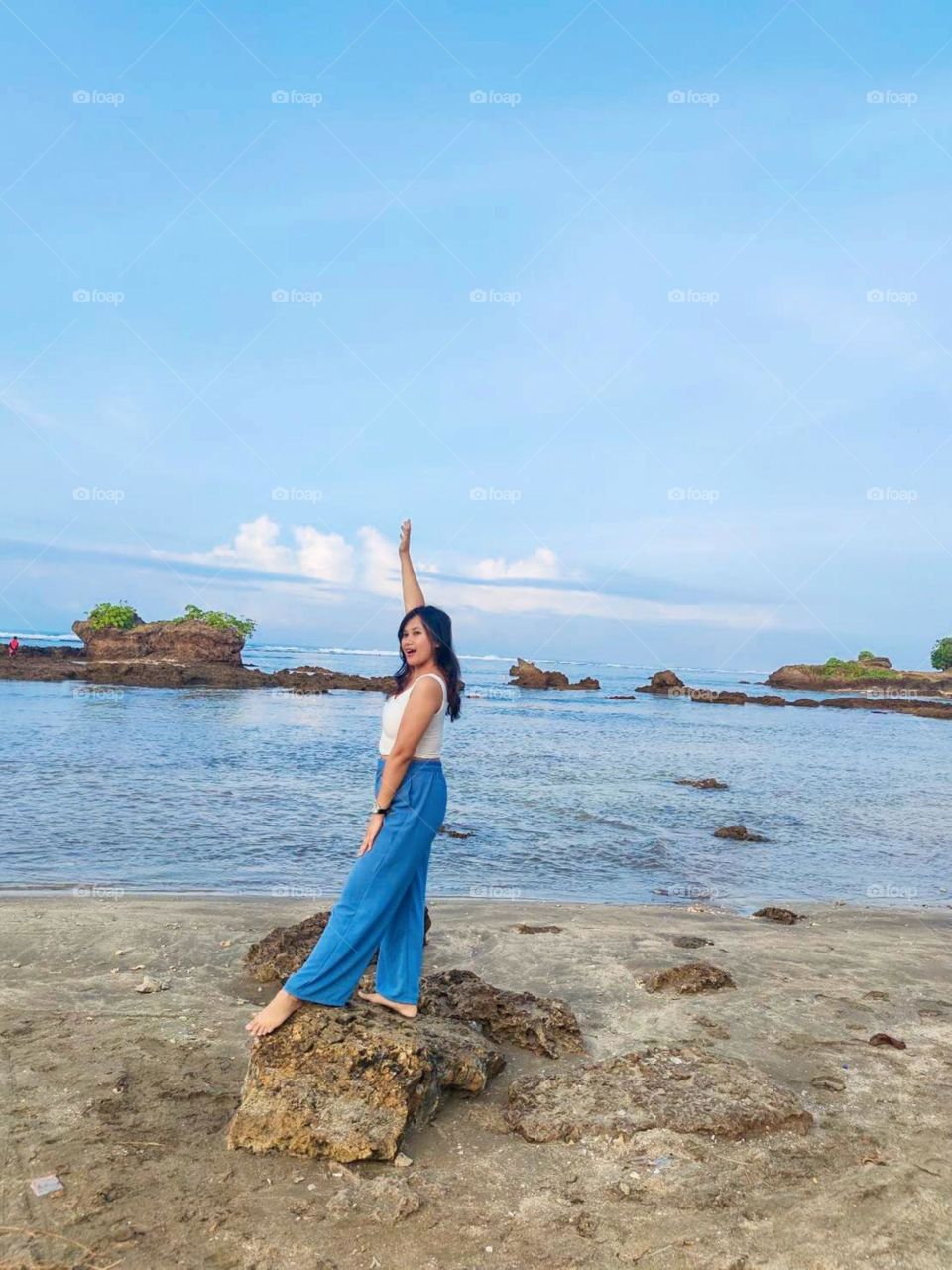 Portrait of a young woman standing on a rocky beach cheerfully