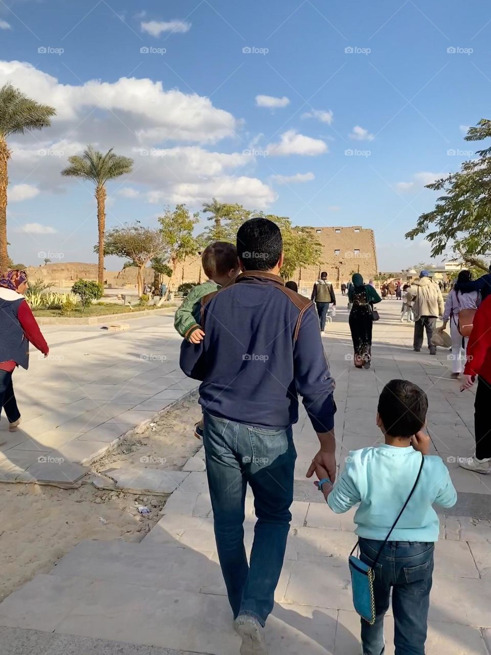 Father holds a son and catches the other one’s hand at Karnak temple in Luxor