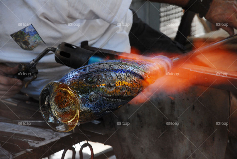A glassblowing artist at work creating a multi colored vase with the additional use of a blow torch!