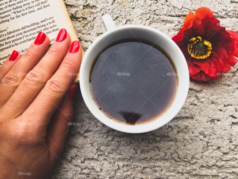 Cup of coffee with a book,a red poppy and a woman's hand