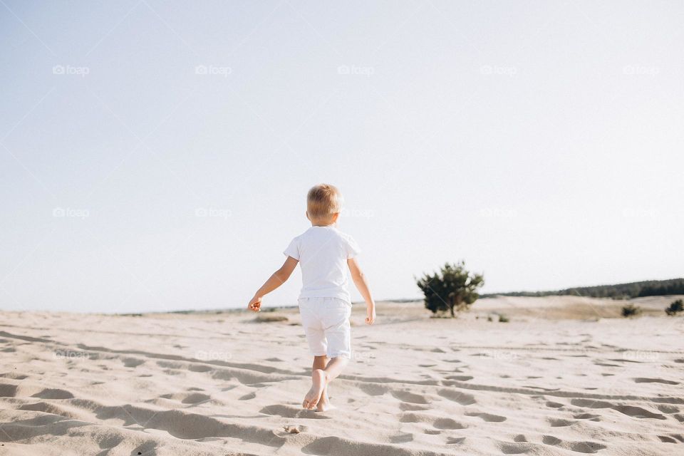 Small boy in white clothes running in sand desert