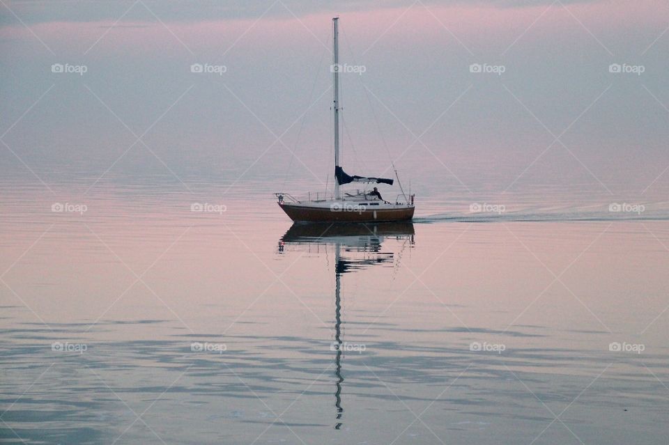 Sailboat sailing in the Great Salt Lake in near glass surface with a simetrical reflection - the sunset casts a pink tie upon the water