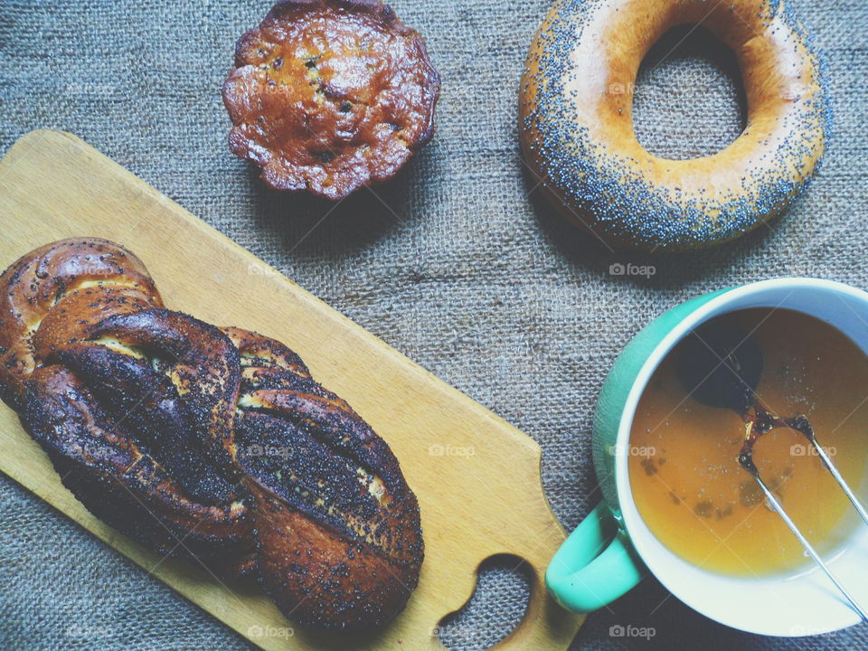 bagel with poppy seeds, basket with poppy seeds, vanilla cupcake and a cup of tea on the table