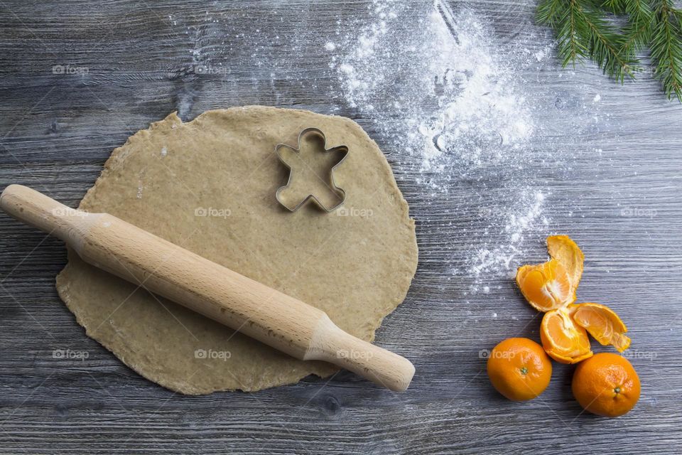 Christmas, gingerbread cookies on a wooden table sprinkled with flour, with tangerines and a green Christmas tree.