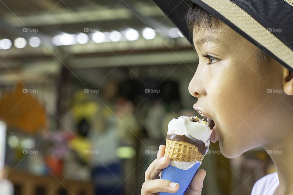 Asian Boys wearing a hat eating ice cream cone in hand.