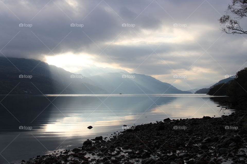 Sun beams coming through the clouds over Loch Lomond in Autumn morning. Plus reflection of mountains