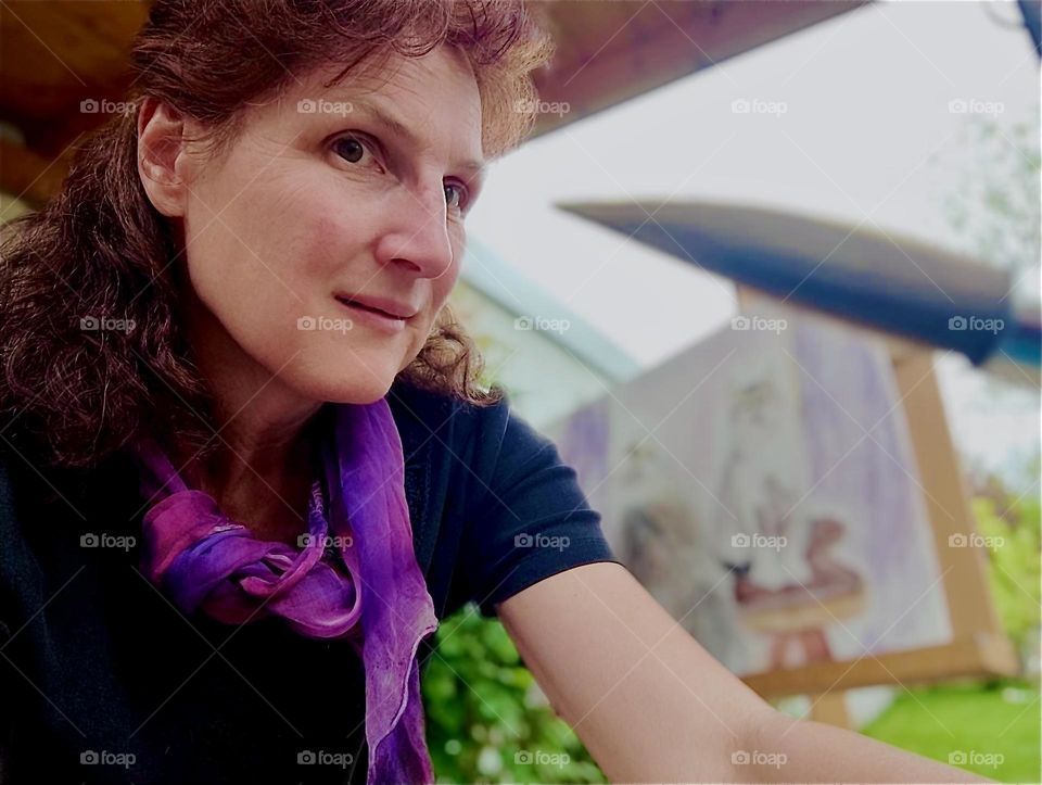 This young lady is drawing a portrait of her two sibling cats “Roukey” and “Linda” from a photo while sitting on the terrace looking out onto the garden of her house in “Bavaria”, Germany where the cats are running around. 2024. Hypnotic Productions