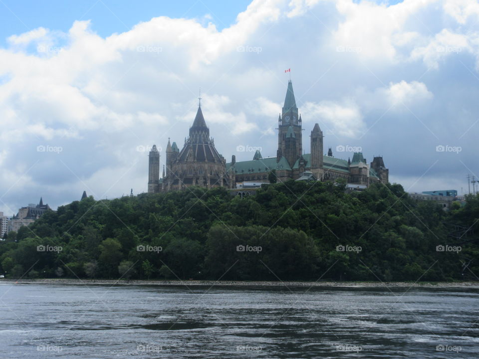 Canadian parliament from the river. Blue sky with clouds and green trees 