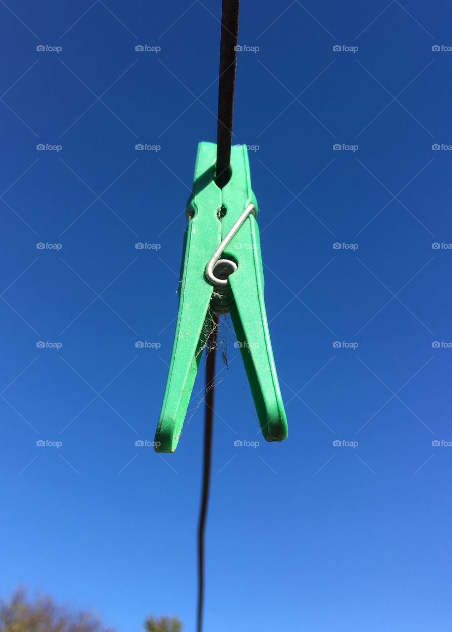 Single green plastic clothespin clothes peg on wire laundry line against vivid blue sky, minimalist, room for text 