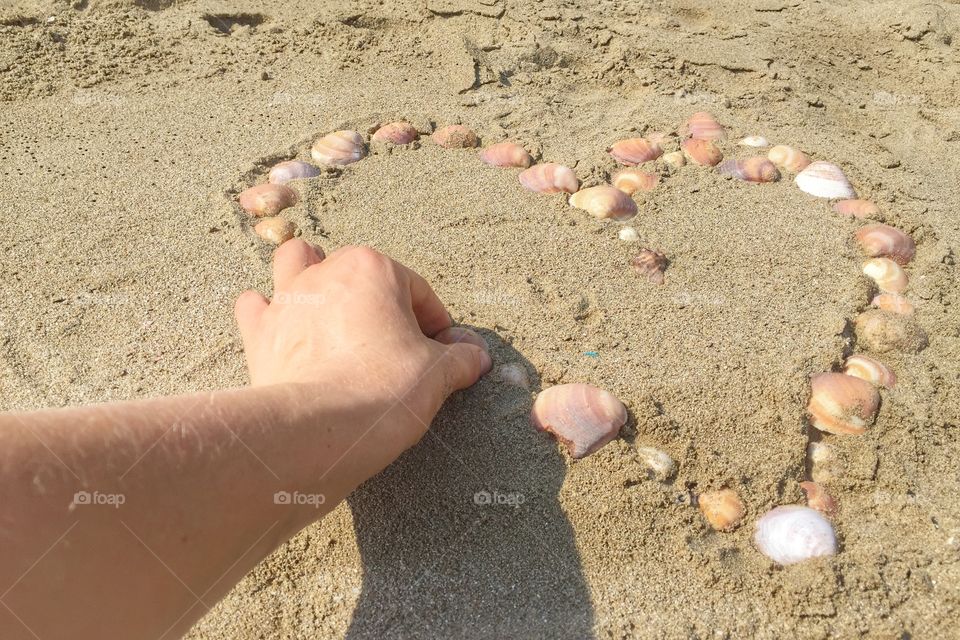 Making a heart shape from shells on the beach 