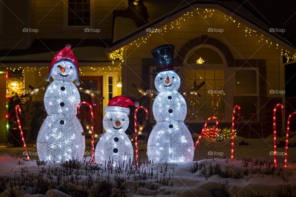 Three glowing snowmen on the house background at night. Christmas lights and decor 