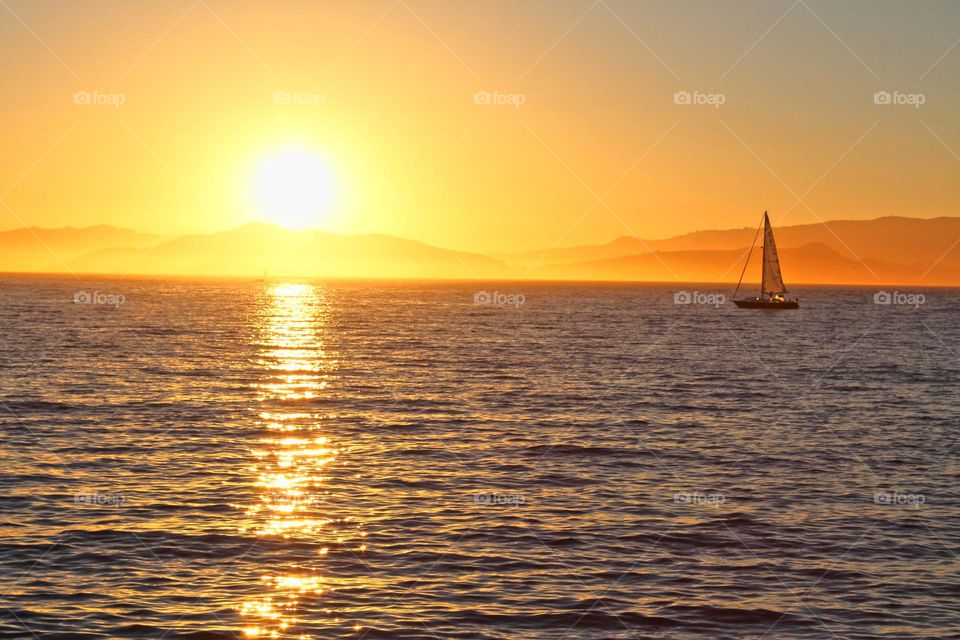enjoying the sunset over the water as a sailboat sells by