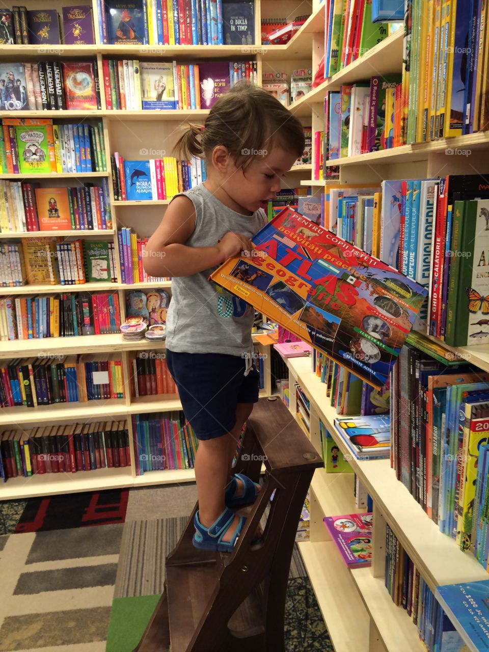 Little girl putting the book in library shelf