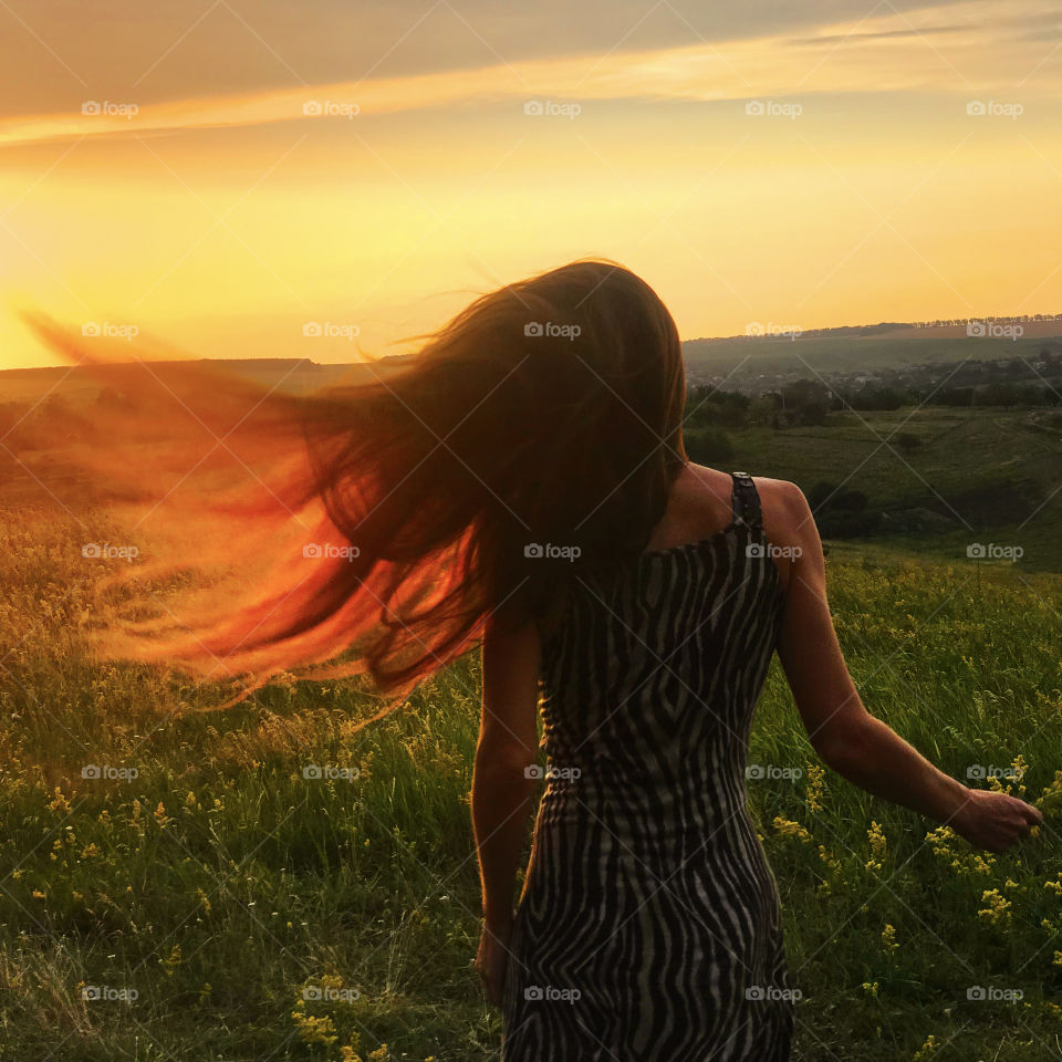 Young woman catching the evening sunlight and wind by her long hair 
