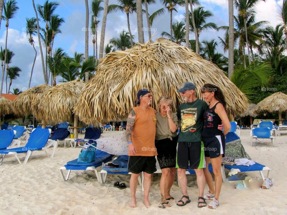 Friends on vacation at a beach resort, standing on the beach shore near palm umbrellas.  Palm trees in background.