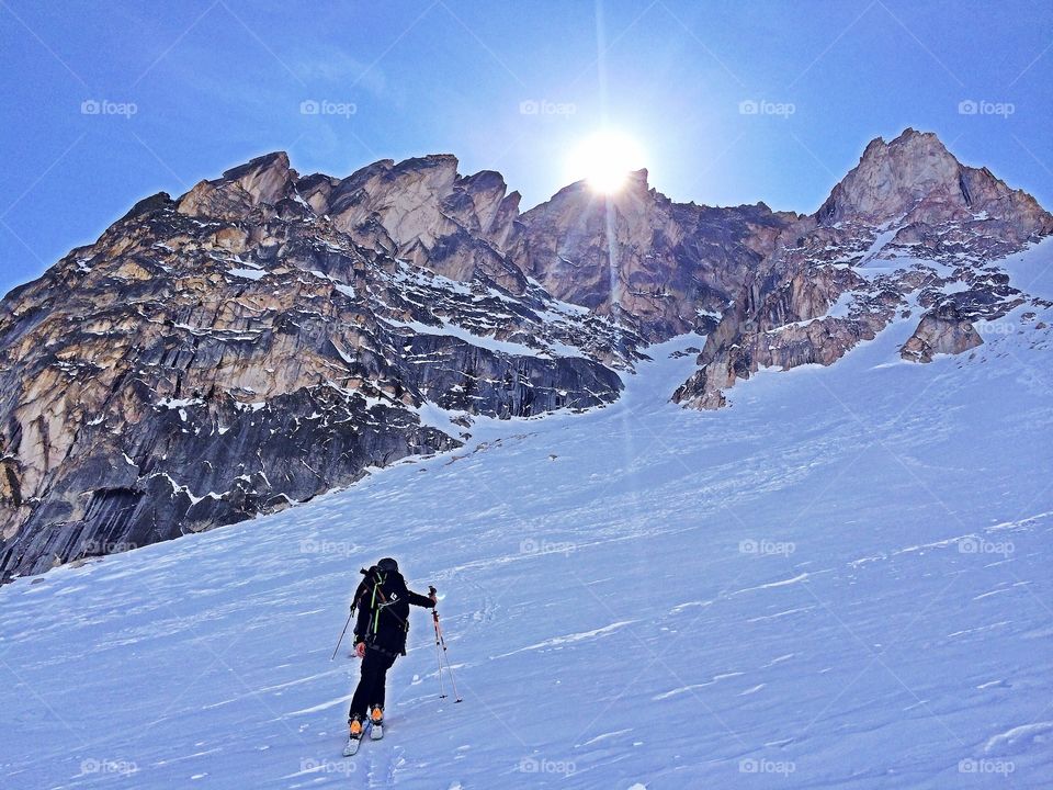 Backcountry skier skinning towards the sunlight and McGowan Peak in the Sawtooth Mountains. 
