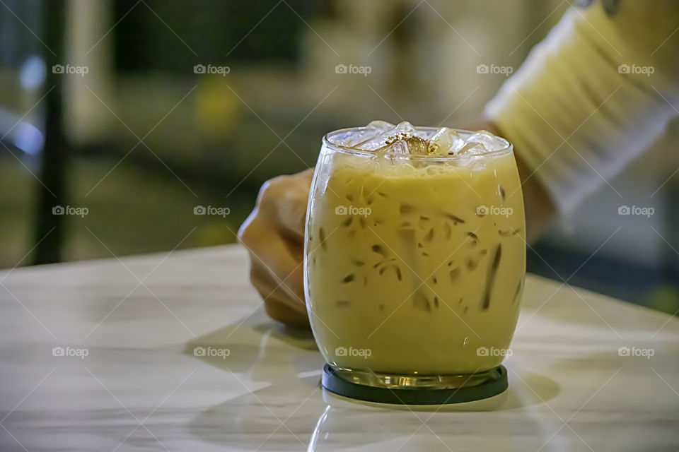 Hand holding Iced coffee in a glass on table.