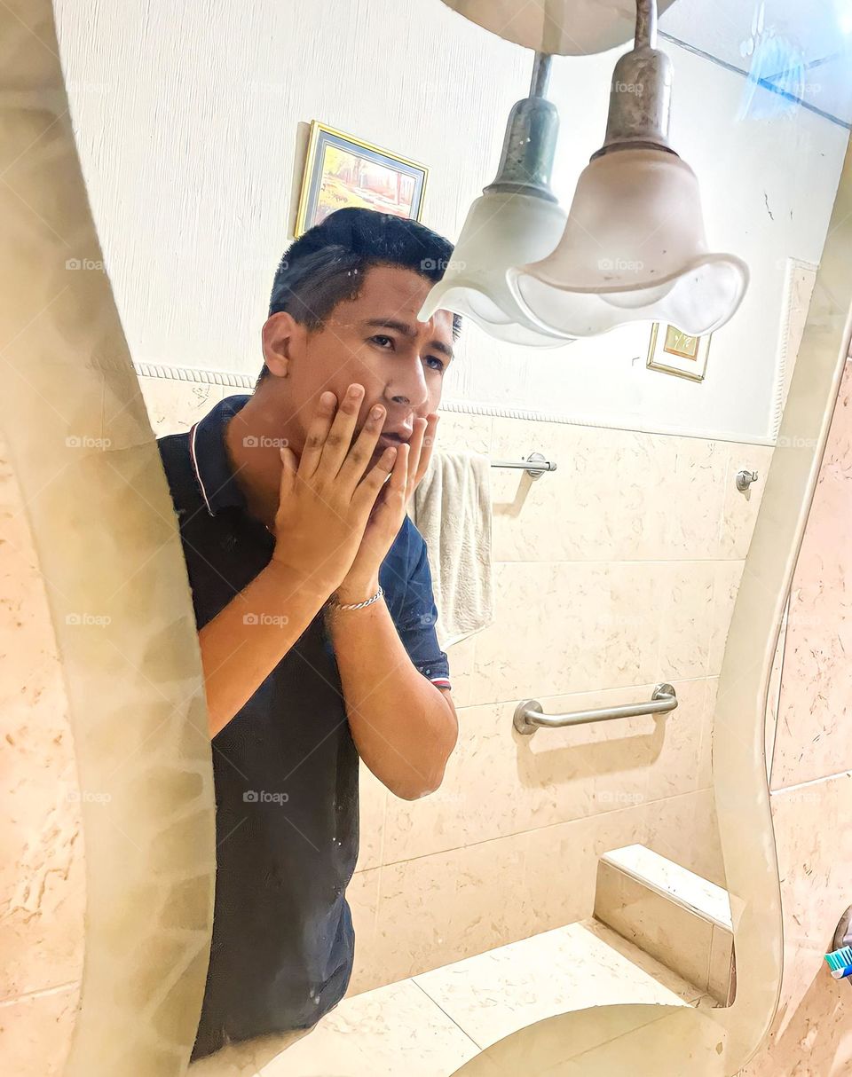 dark-skinned man observing the skin of his face in the bathroom mirror, touching his chin with his two hands, with an anguished expression