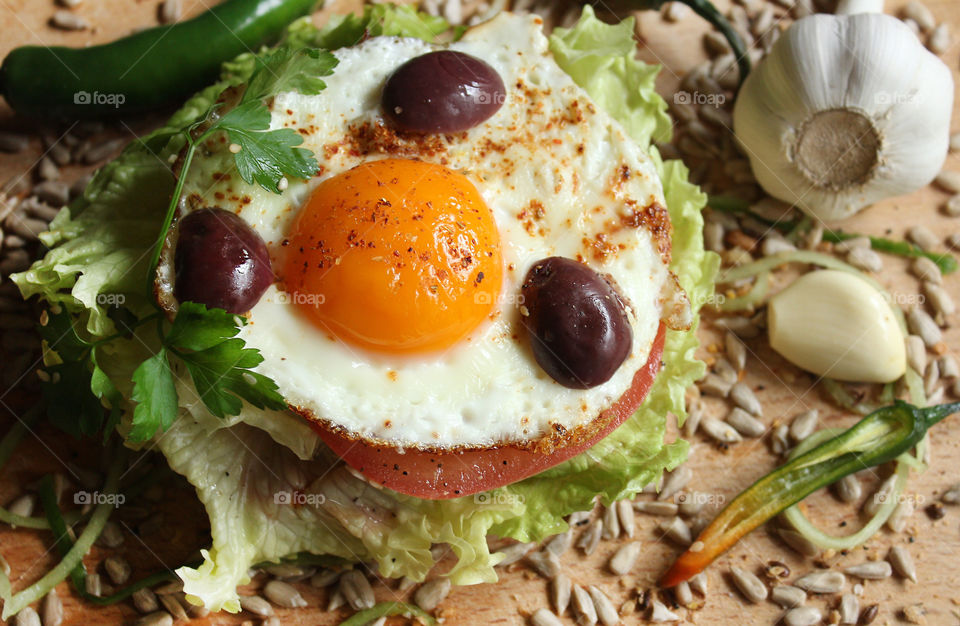 Tasty burger with fried egg, olives, lettuce, seeds, hot pepper, garlic