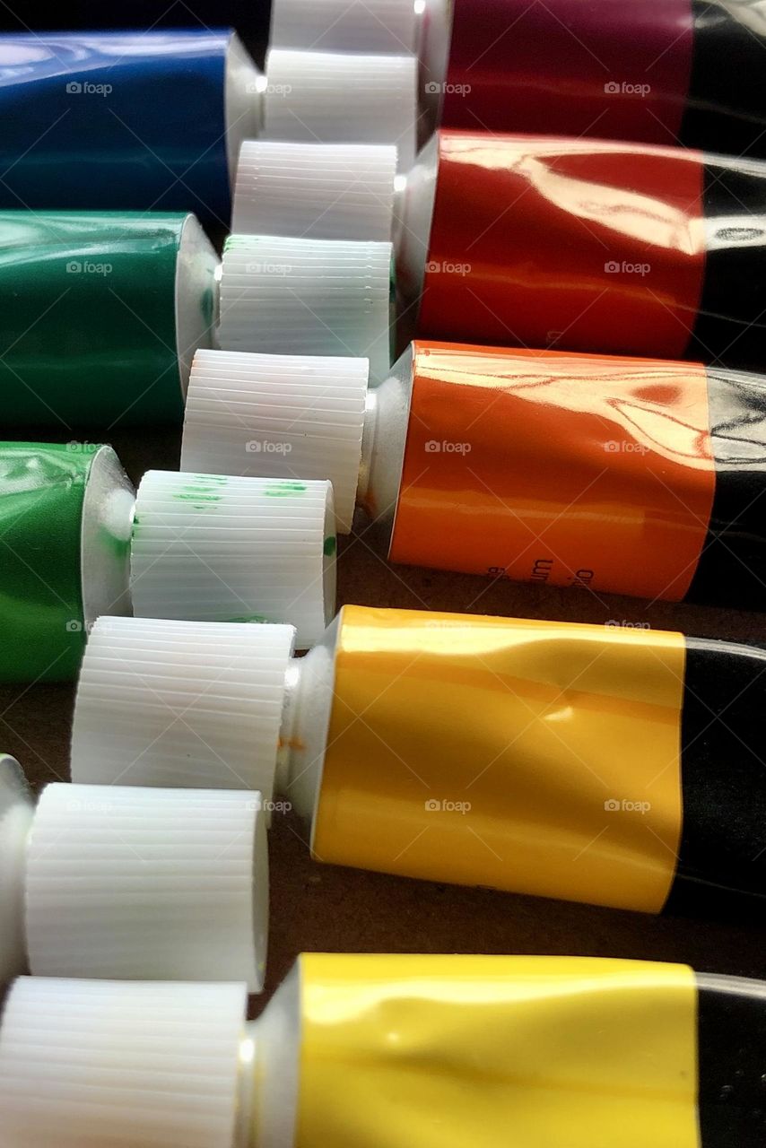 Closeup row of tubes of oil paints, focused on warm autumn tones in yellow, orange and red.