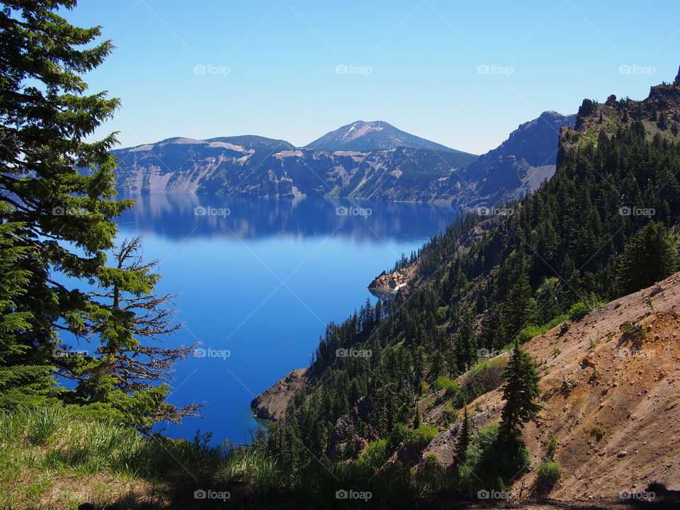 The rugged rim reflect in the stunning rich blue waters of Crater Lake in Southern Oregon on beautiful sunny summer morning. 