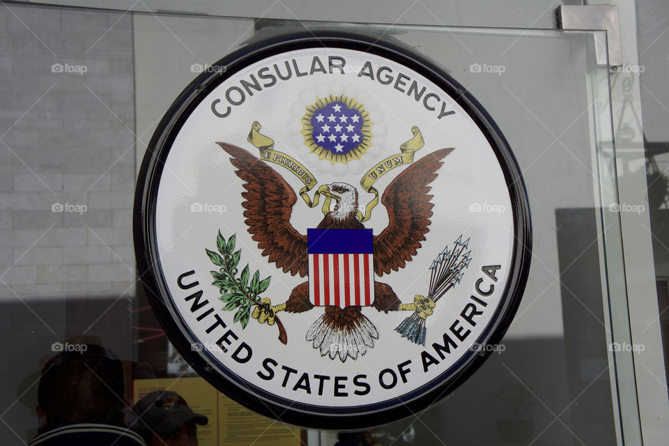 A United States Consular Agency sign and logo in the window of their office in San Miguel de Allende, Mexico. A consul provides official representative of the government of one country in the territory of another.