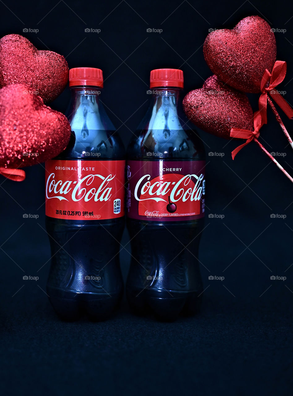 Close up shot of two Coca Cola with black background with the mists at the studio with hearts. 