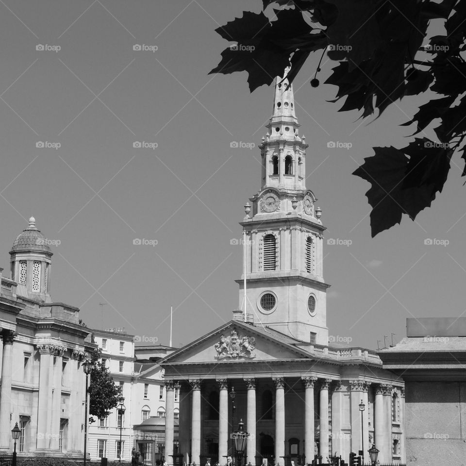 An old ornate building with a clock in its tower, many pillars, and decorative carvings on a sunny summer day in London. 