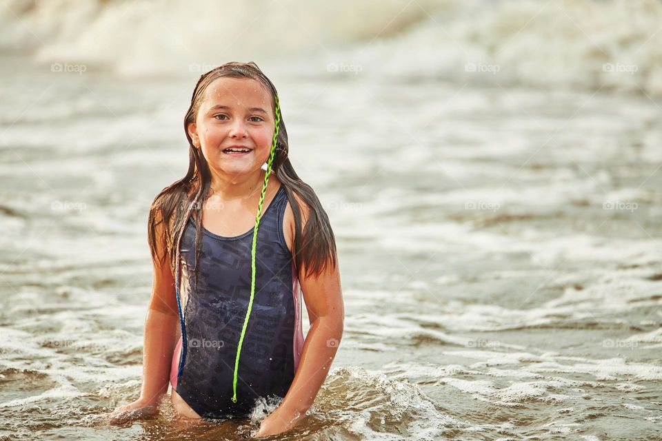 Little girl playing with waves in the sea. Kid playfully splashing in waves. Child jumping in sea. Vacations on the beach. Water splashes. Fun and play during summer vacation. Travel concept