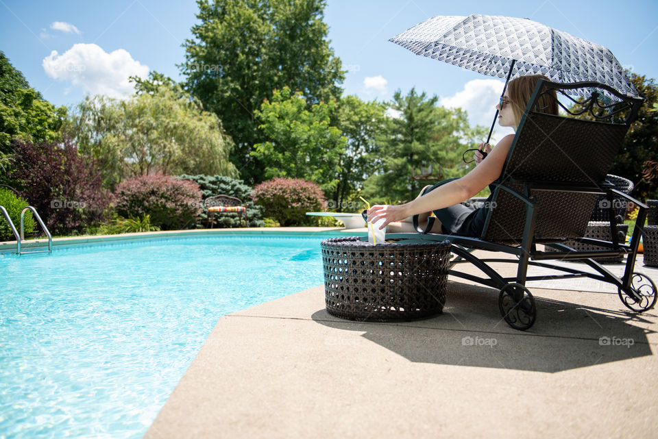 Millennial woman lounging poolside with an umbrella 