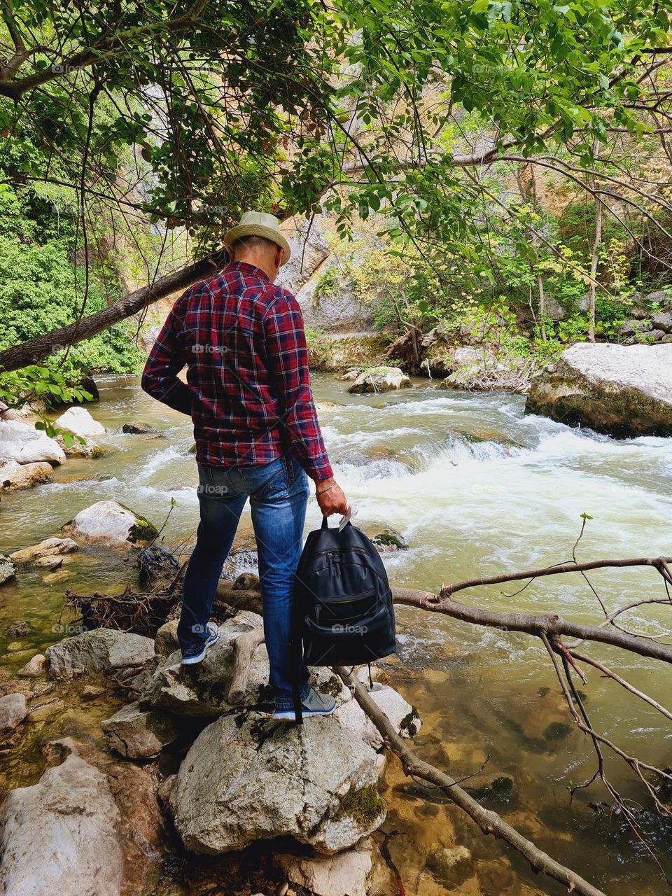 Shoulders hiker with warm checkered flannel shirt and backpack standing on the river bank