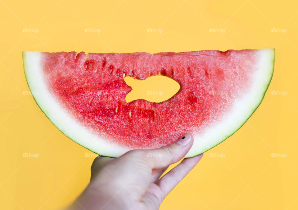 A hand holding a watermelon slice with fish shaped hole