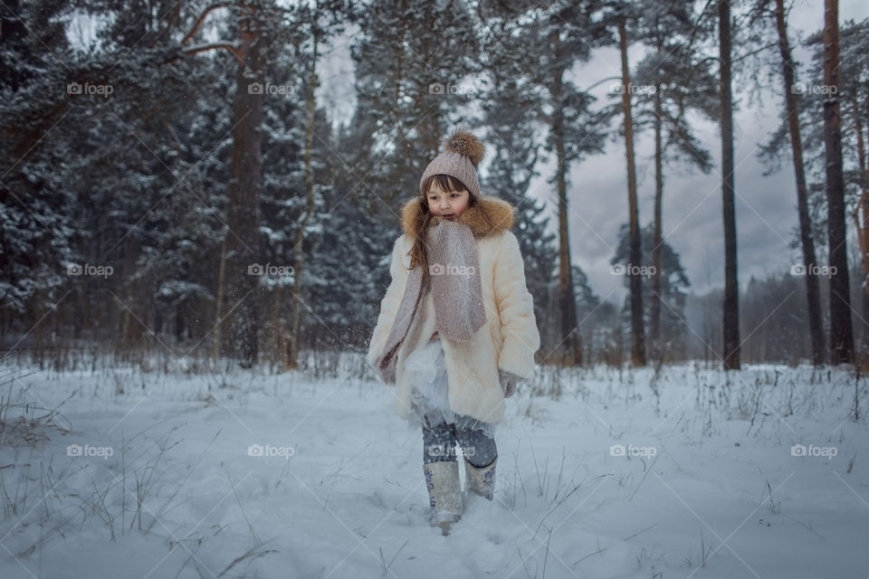 Winter forest at cloudy day. Little girl walking