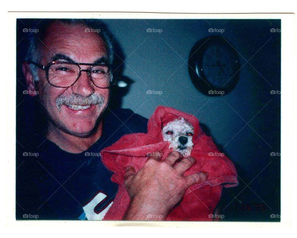Happy smiling man holding puppy wrapped up in a towel after a bath. All you see is a little white puppy face.