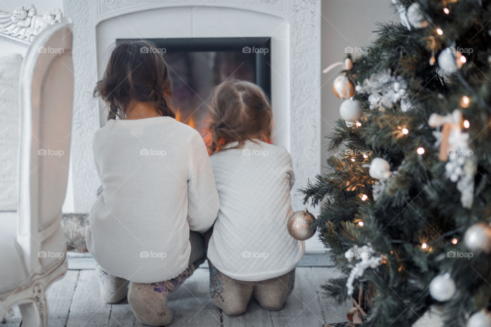 Little girls in wool boots near fireplace and Christmas tree 