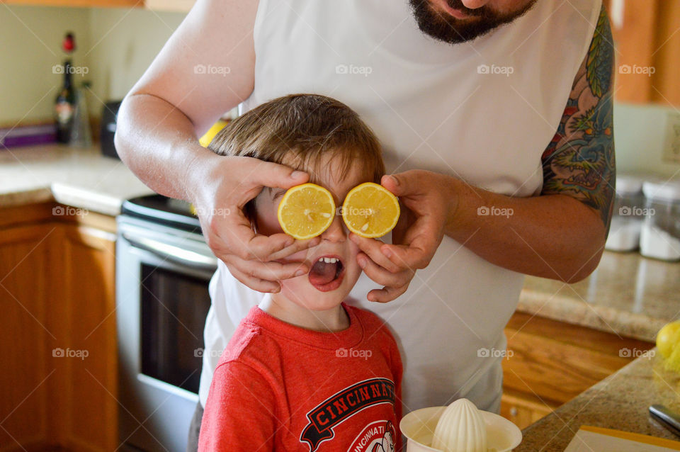 Father holding two lemon halves as son's eyes while cooking in the kitchen