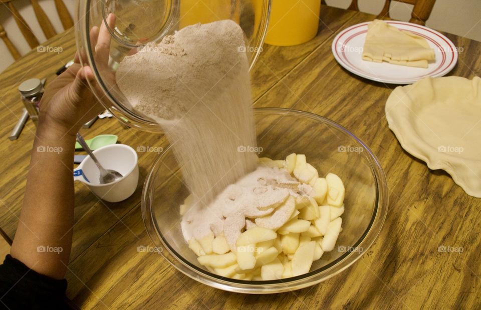 Pouring sugar and cinnamon onto apples to make a pie 