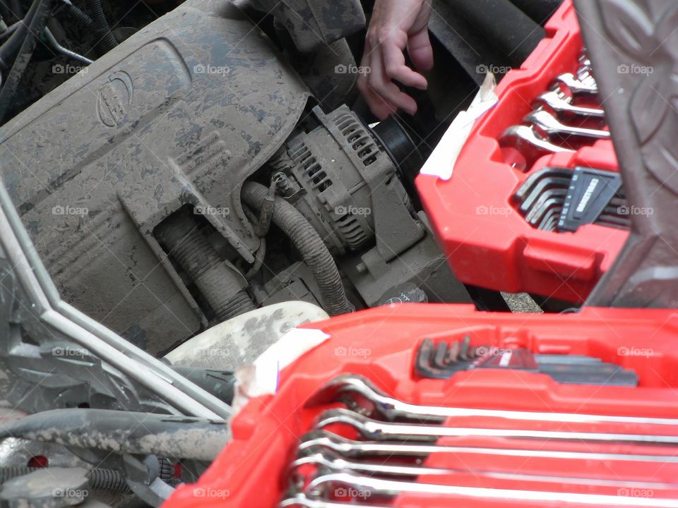 Under the hood of a red pickup truck with combination wrench set tools organized in a red tool hard case by the work station with its reflection from a mirror and the mechanic handyman fixing a piece.