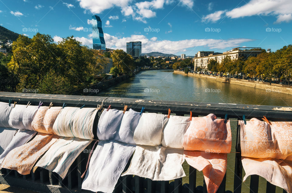 Fabrics, embroidery and scarves for sale on the railing of Dry bridge of flea market against Kura River, Tbilisi, Georgia.