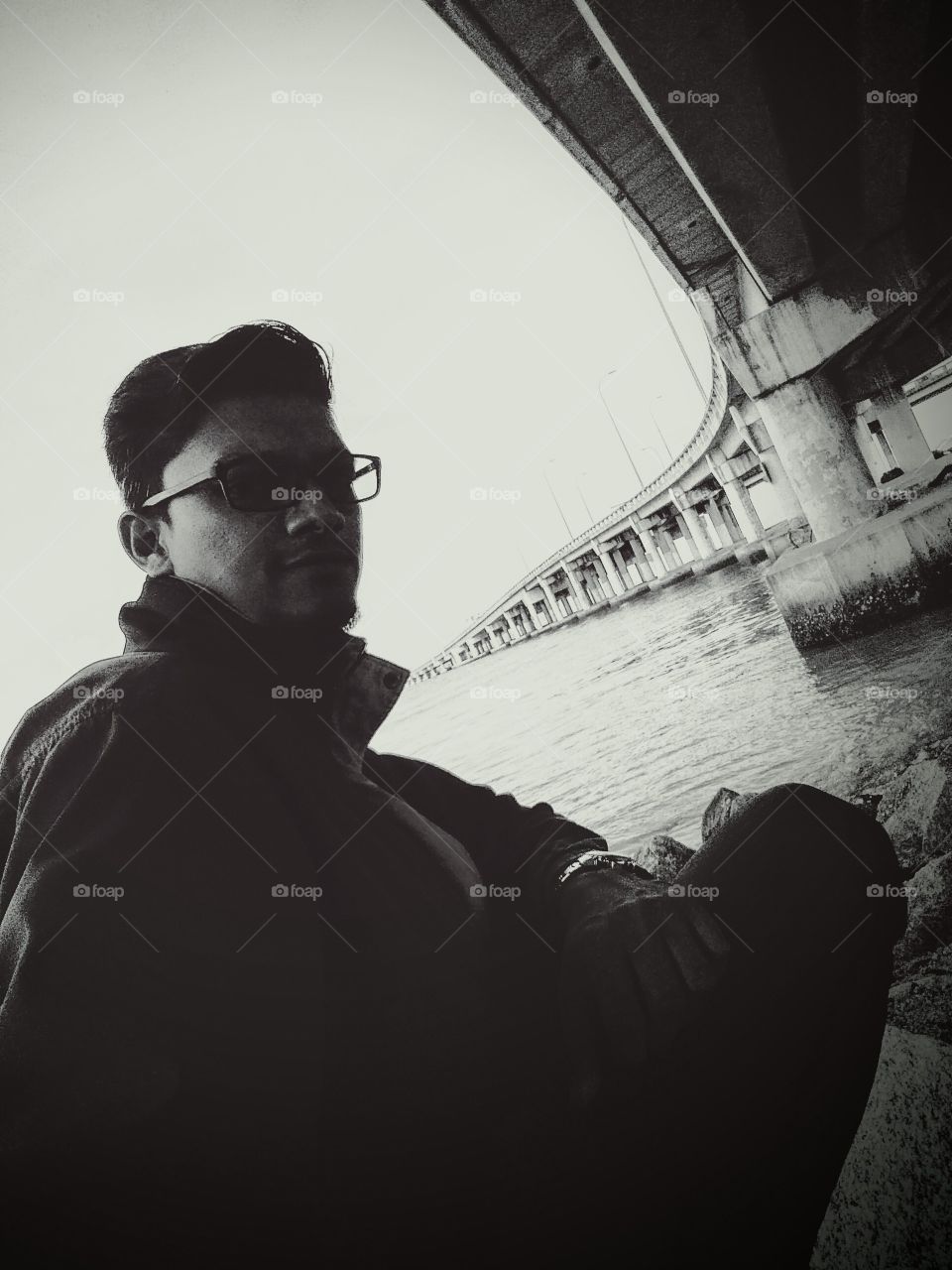 A man sitting at sea shore near bridge