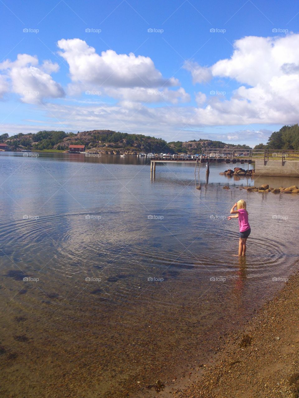 little girl standing in the sea and throwing a seashell into the sea in summertime