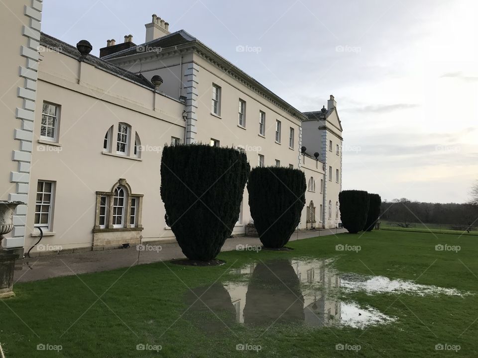 Side view of this beautiful stately home, the added attraction being the reflective view of the large conifers, from the grassland puddles.