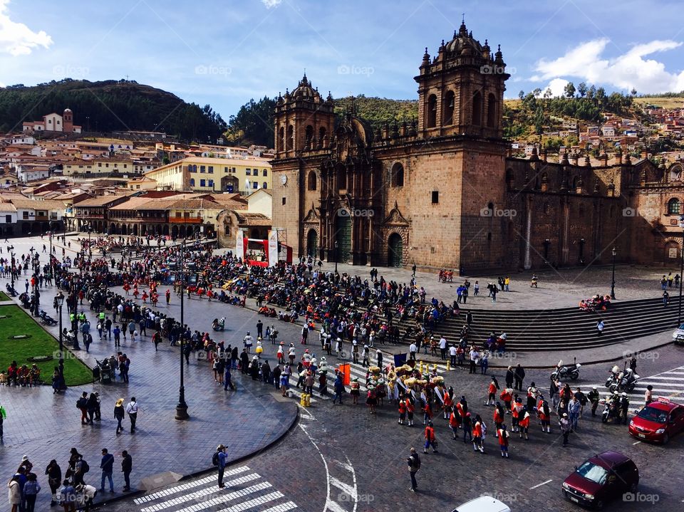 An aerial view of crowds moving past an old cathedral in Cuzco’s main square on a sunny day. 
