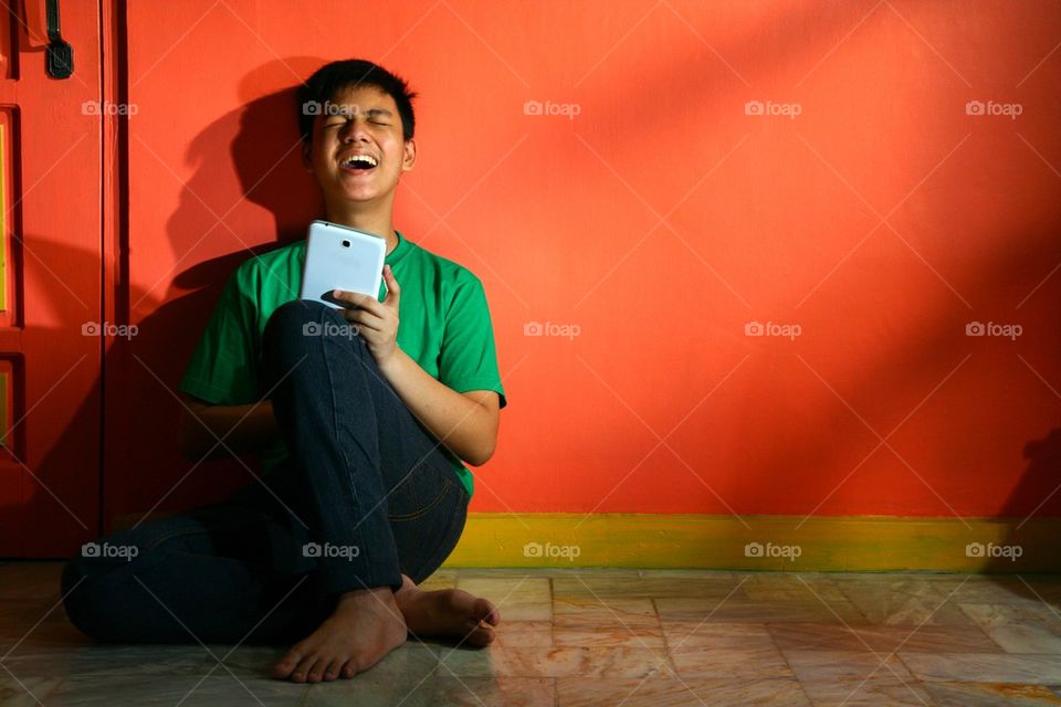 young asian teen with a tablet in a living room and laughing